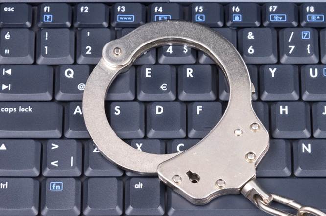 A pair of handcuffs rests atop a keyboard, symbolizing criminal justice in the digital age. The keyboard letters are clearly visible under the metal of the cuffs.